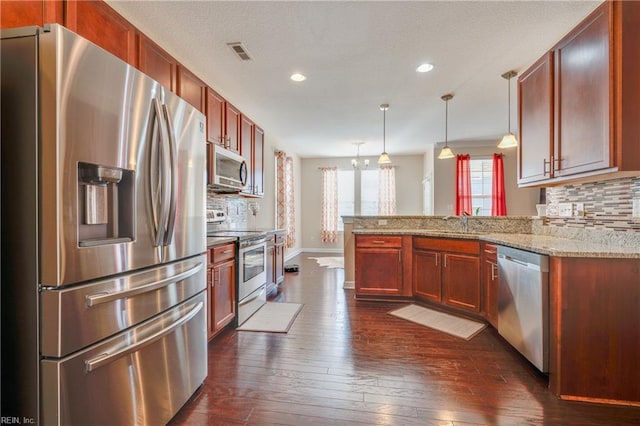 kitchen featuring light stone counters, dark hardwood / wood-style flooring, kitchen peninsula, decorative light fixtures, and appliances with stainless steel finishes