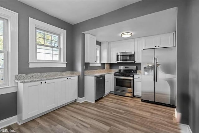 kitchen with light stone countertops, light hardwood / wood-style flooring, white cabinets, and stainless steel appliances