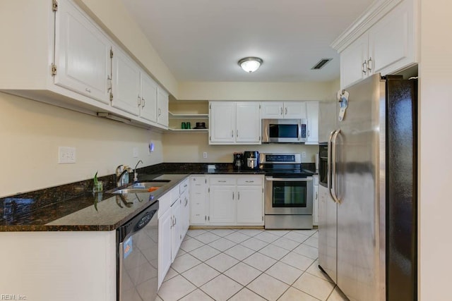 kitchen with sink, stainless steel appliances, light tile patterned floors, dark stone counters, and white cabinets