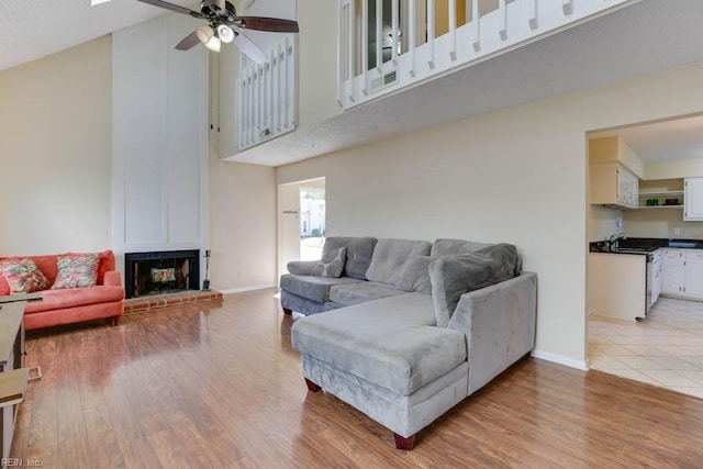 living room with light wood-type flooring, high vaulted ceiling, a brick fireplace, and ceiling fan