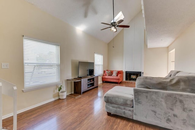 living room featuring ceiling fan, high vaulted ceiling, a textured ceiling, a fireplace, and hardwood / wood-style flooring