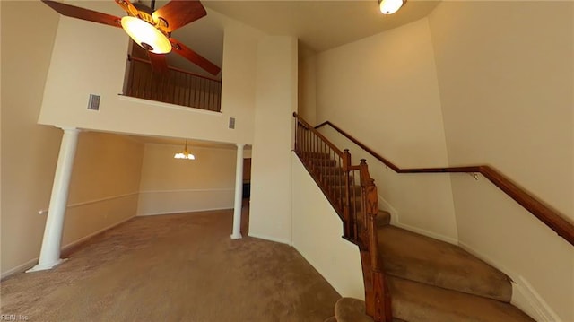 stairway featuring carpet flooring, a high ceiling, ceiling fan with notable chandelier, and decorative columns