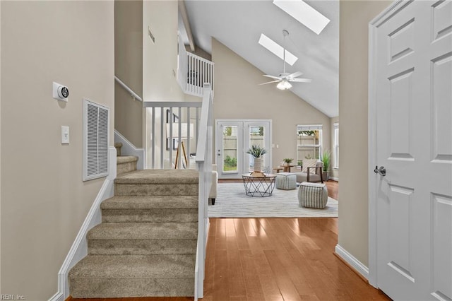 staircase featuring a skylight, high vaulted ceiling, hardwood / wood-style flooring, and ceiling fan