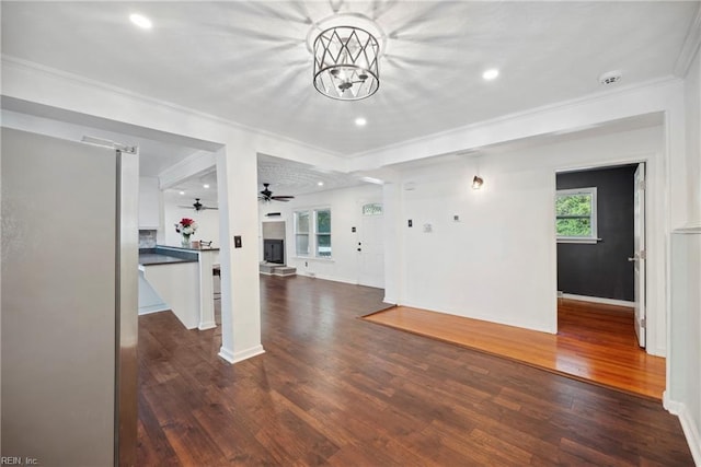 unfurnished living room featuring ceiling fan with notable chandelier, crown molding, and dark wood-type flooring