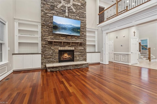 unfurnished living room with hardwood / wood-style floors, built in shelves, a fireplace, and a high ceiling