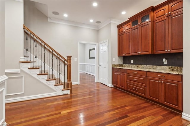 kitchen with decorative backsplash, dark hardwood / wood-style flooring, light stone countertops, and crown molding