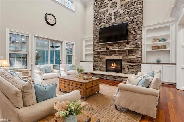 living room featuring hardwood / wood-style floors, built in features, a towering ceiling, and a fireplace