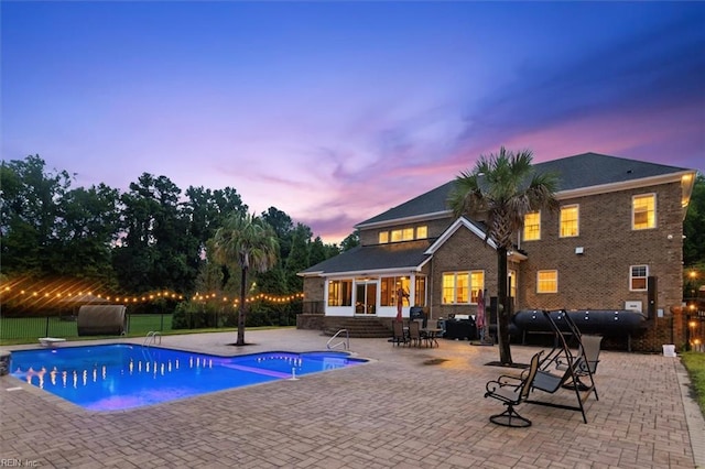 pool at dusk with a patio area and a diving board
