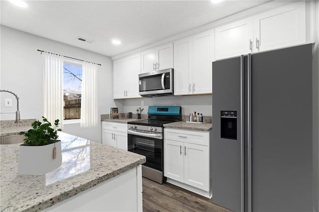 kitchen featuring sink, dark hardwood / wood-style floors, appliances with stainless steel finishes, light stone counters, and white cabinetry