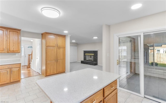 kitchen with a center island, ornamental molding, light tile patterned floors, and a brick fireplace