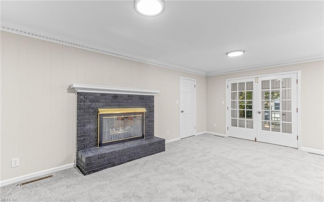 unfurnished living room with crown molding, french doors, light colored carpet, and a brick fireplace