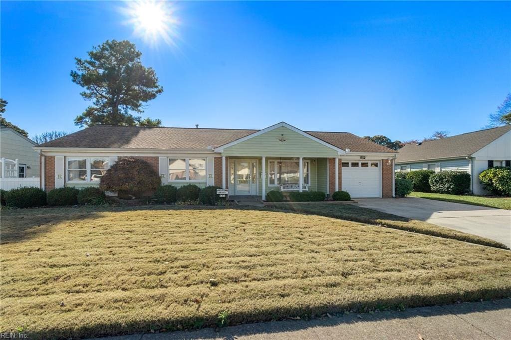 single story home with covered porch, a garage, and a front lawn