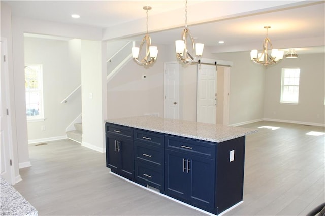 kitchen featuring a barn door, light stone counters, pendant lighting, and light hardwood / wood-style floors