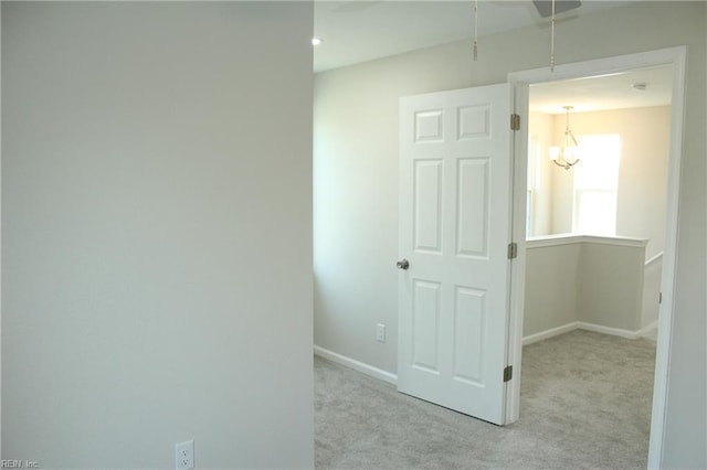 corridor with light colored carpet and a notable chandelier