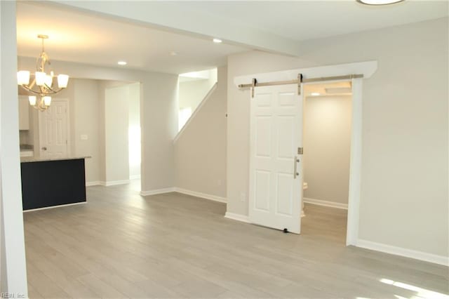 spare room with a barn door, an inviting chandelier, and light wood-type flooring