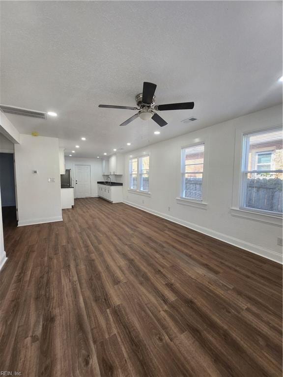 unfurnished living room with a textured ceiling, dark hardwood / wood-style flooring, plenty of natural light, and ceiling fan