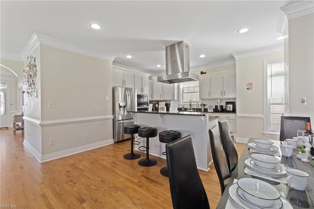 kitchen with light hardwood / wood-style flooring, ornamental molding, island range hood, white cabinetry, and stainless steel appliances