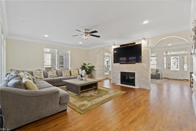 living room with ceiling fan, a stone fireplace, crown molding, and light hardwood / wood-style flooring