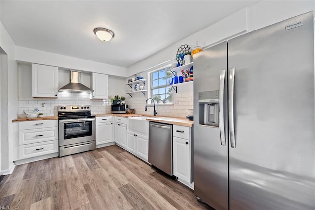 kitchen featuring wall chimney exhaust hood, butcher block counters, white cabinetry, and stainless steel appliances