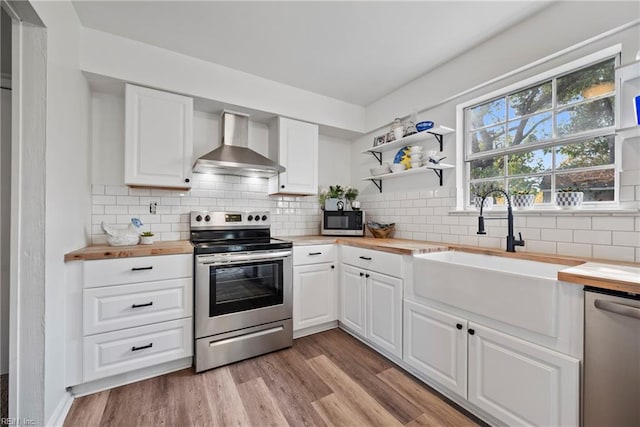 kitchen with sink, stainless steel appliances, wall chimney range hood, wooden counters, and white cabinets