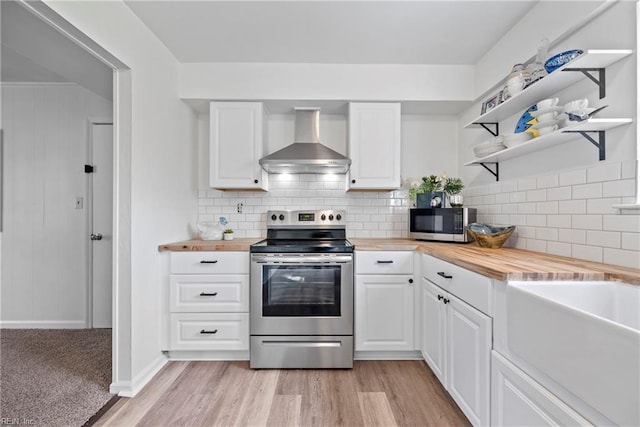 kitchen with butcher block countertops, white cabinetry, wall chimney range hood, and appliances with stainless steel finishes