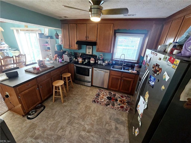 kitchen with kitchen peninsula, appliances with stainless steel finishes, a textured ceiling, ceiling fan, and sink