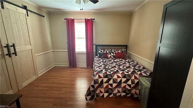 bedroom featuring a barn door, ceiling fan, crown molding, and wood-type flooring