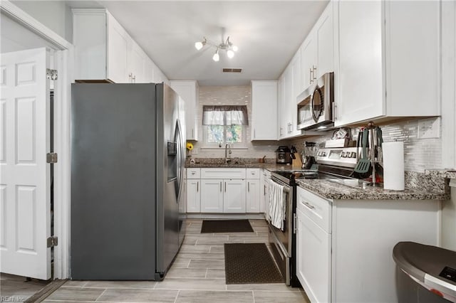 kitchen with sink, dark stone countertops, appliances with stainless steel finishes, white cabinets, and light wood-type flooring