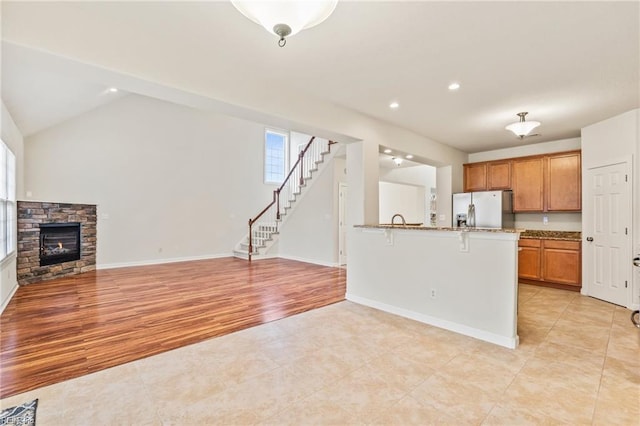 kitchen with a stone fireplace, stainless steel fridge, vaulted ceiling, a breakfast bar area, and light wood-type flooring