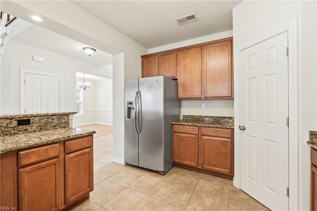 kitchen with a chandelier, stainless steel refrigerator with ice dispenser, dark stone counters, and light tile patterned flooring