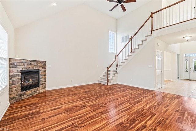 unfurnished living room featuring hardwood / wood-style flooring, ceiling fan, a stone fireplace, and high vaulted ceiling