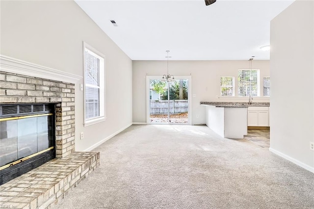 unfurnished living room featuring light carpet, a fireplace, sink, and a notable chandelier