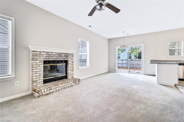 unfurnished living room with ceiling fan with notable chandelier, carpet floors, and a brick fireplace