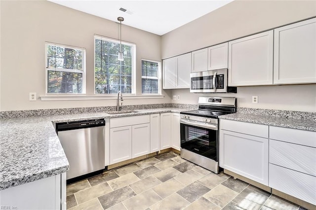 kitchen featuring light stone countertops, stainless steel appliances, sink, white cabinets, and hanging light fixtures