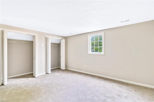 unfurnished bedroom with light carpet and two closets