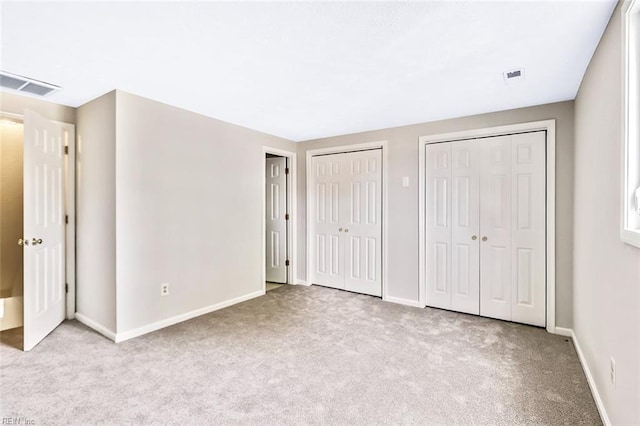 unfurnished bedroom with two closets and light colored carpet