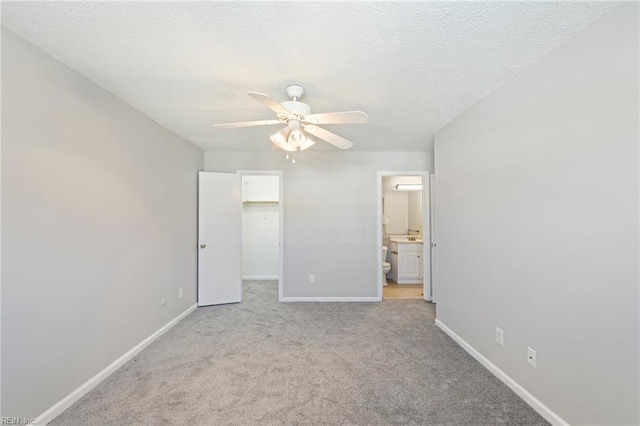 unfurnished bedroom featuring light carpet, ensuite bath, ceiling fan, a spacious closet, and a closet