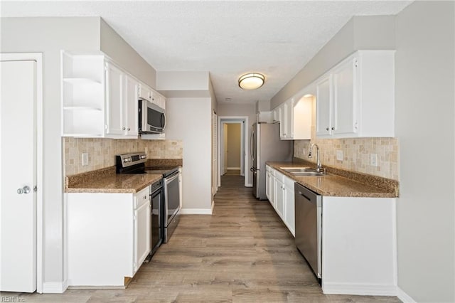 kitchen featuring white cabinetry, sink, stainless steel appliances, dark stone counters, and light hardwood / wood-style floors