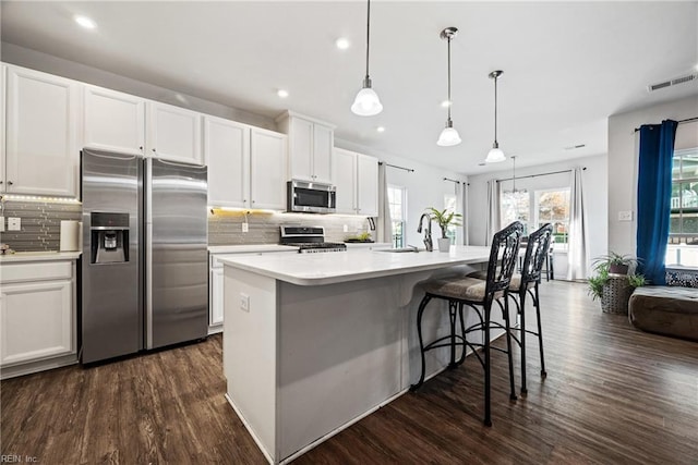 kitchen featuring a center island with sink, white cabinets, appliances with stainless steel finishes, decorative light fixtures, and dark hardwood / wood-style flooring