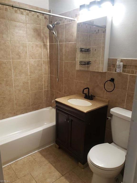 full bathroom with vanity, toilet, tiled shower / bath, and tile walls