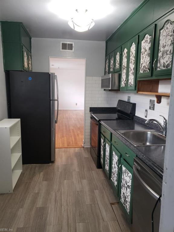 kitchen with backsplash, sink, black appliances, hardwood / wood-style floors, and green cabinets