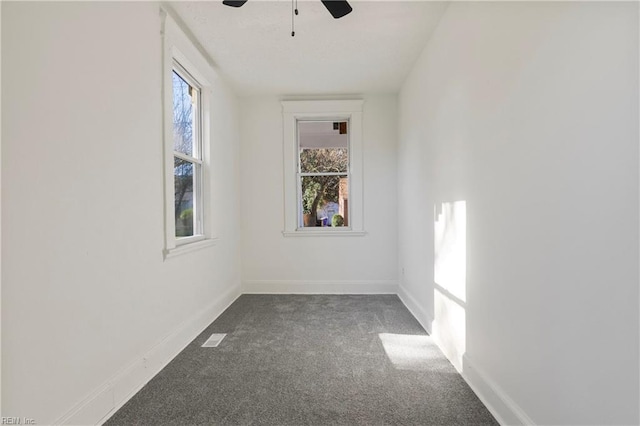 unfurnished room featuring ceiling fan, a healthy amount of sunlight, and dark colored carpet