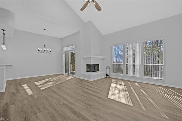 unfurnished living room with wood-type flooring, ceiling fan with notable chandelier, and high vaulted ceiling