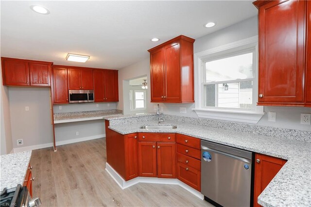 kitchen featuring light stone countertops, stainless steel appliances, ceiling fan, sink, and light hardwood / wood-style flooring