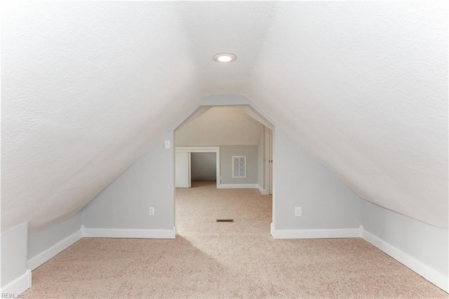 bonus room featuring a textured ceiling, light colored carpet, and vaulted ceiling