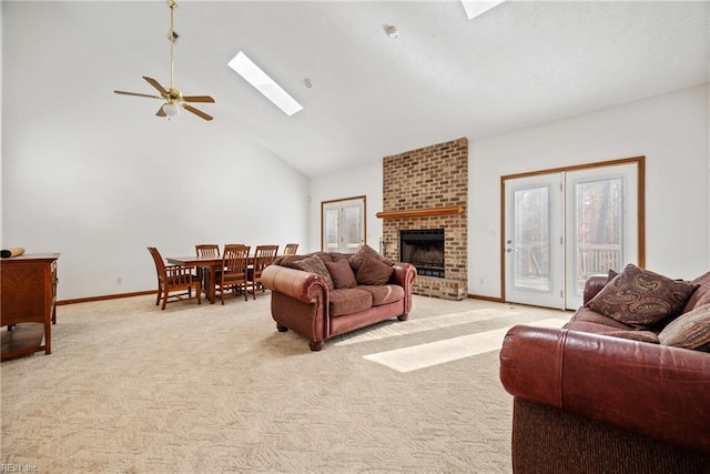 carpeted living room featuring ceiling fan, a skylight, high vaulted ceiling, and a brick fireplace