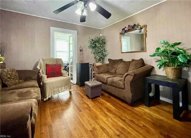 living room with ceiling fan, wood-type flooring, a textured ceiling, and ornamental molding