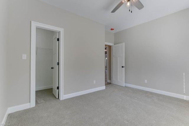 unfurnished bedroom featuring light carpet, a walk in closet, a closet, and ceiling fan