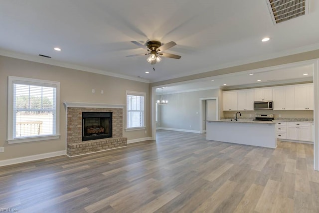 unfurnished living room with a fireplace, sink, light wood-type flooring, and crown molding