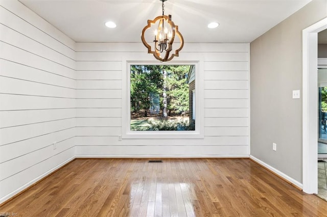 unfurnished dining area featuring wood walls, wood-type flooring, and an inviting chandelier